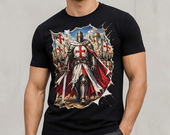 May include: A black t-shirt featuring a graphic print of a knight in silver armor wearing a white tabard with a red cross and a flowing red cape. The knight holds a sword, standing before a background of flags with red crosses and stone structures.