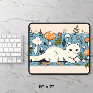May include: A rectangular mousepad with a whimsical illustration of a white cat lounging amidst cartoon mushrooms, flowers, and foliage. The mousepad measures 9 inches by 7 inches. The design features a light blue background with a cream-colored border.