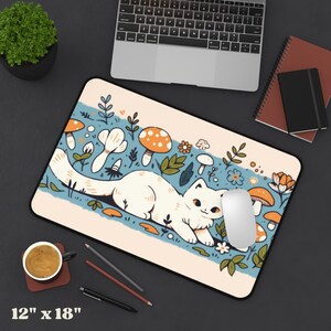 May include: A rectangular mouse pad with a whimsical design featuring a white cat, mushrooms, and flowers. The pad measures 12 inches by 18 inches and has a black border. A computer mouse rests on the pad.