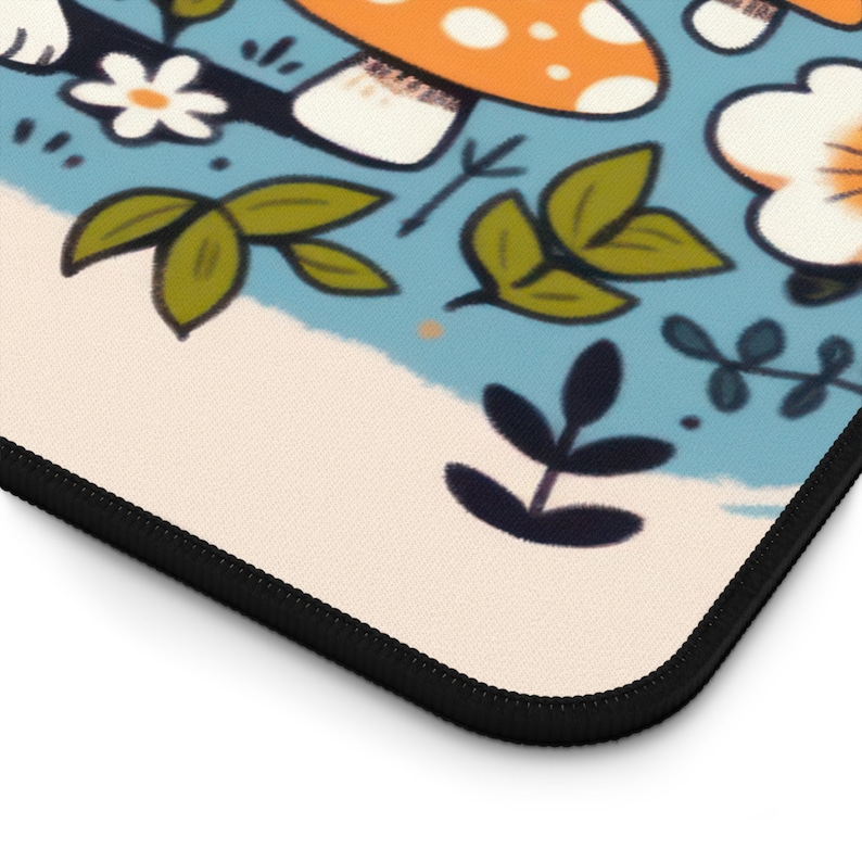 May include: A rectangular mousepad with a whimsical illustration. The design features orange mushrooms with white spots, white flowers, and green leaves against a light blue and cream background. The mousepad has a black stitched edge.