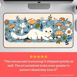 May include: A rectangular mouse pad featuring a white cat lounging amidst orange-capped mushrooms, flowers, and foliage on a light blue background. The design has a whimsical, cartoonish style. The pad has a black border.