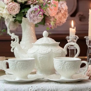 Può includere: Servizio da tè in porcellana bianca con intricati motivi floreali. Il set comprende una teiera, due tazze da tè e due piattini.