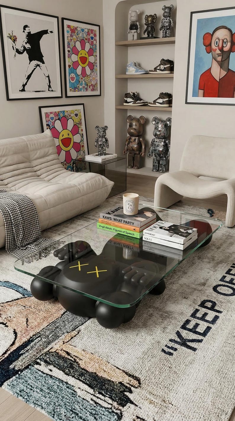 Pode incluir: Uma sala de estar moderna com uma mesa de centro preta com base de figura KAWS e tampo de vidro. O quarto inclui obras de arte, figuras decorativas, um tapete com texto e um sof&aacute; branco.