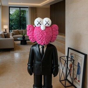 May include: A large, black sculpture of a figure in a suit with a pink, furry head and white eyes with black X's. The figure is standing in a modern, well-lit living room. A framed artwork and a black metal geometric sculpture are visible.