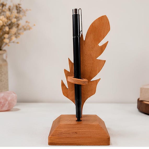 Cherry wood pen holder carved into a feather quill silhouette — whimsical, writer-coded, and genuinely beautiful as a desk sculpture.