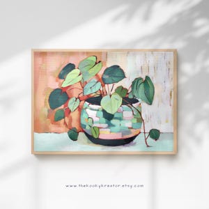 Puede incluir: Pintura abstracta de una planta en maceta con hojas en forma de corazón. La maceta es una mezcla de verde azulado, rosa y blanco, y el fondo presenta tonos melocotón y crema. La obra de arte está enmarcada en un marco de madera clara. El sitio web www.thekookykreator.etsy.com está en la parte inferior.