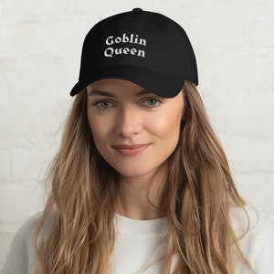 May include: Black baseball cap with the embroidered text "Goblin Queen" in white. The cap has a curved brim and a classic six-panel design. The hat is made of a durable fabric.