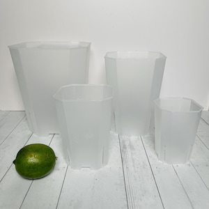 May include: Four clear plastic octagonal pots of varying sizes. The pots are on a white wooden surface.