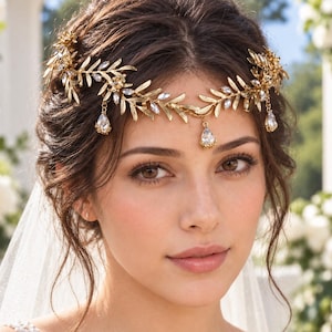 May include: A gold-toned metal headpiece featuring a delicate leaf and vine design adorned with small clear crystals. The accessory includes three dangling teardrop-shaped crystals that hang from the leafy branches across the forehead.