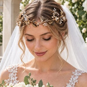May include: A gold-toned hair vine featuring metallic leaves, small clear crystals, and delicate floral accents. The headpiece is worn across the forehead and temples, paired with a sheer white veil that drapes over the shoulders and back.
