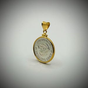 May include: A gold pendant with a silver coin. The coin is inscribed with "AUSTRALIA" and "SHILLING 1963". The coin is set in a gold bezel with a gold loop for a chain.