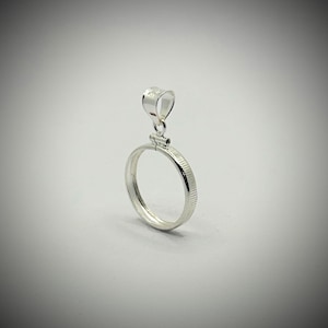 Op de afbeelding: Een zilveren hanger met een cirkelvormig frame en een getextureerde rand. De hanger heeft een kleine lus aan de bovenkant voor een ketting. Het ontwerp is eenvoudig en elegant, geschikt voor dagelijks gebruik.
