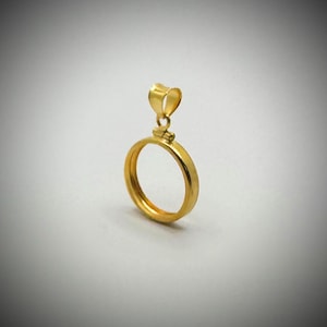 Op de afbeelding: Een goudkleurige hanger met een cirkelvormig frame en een hartvormige lus. De hanger is gemaakt van glanzend metaal en staat tegen een zachte, neutrale achtergrond. Het ontwerp is eenvoudig en elegant.