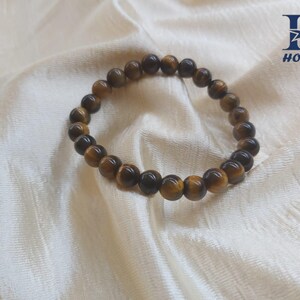 May include: A beaded bracelet made of tiger's eye gemstones. The bracelet features round, polished beads in shades of brown and gold. The bracelet is displayed on a white, textured fabric.