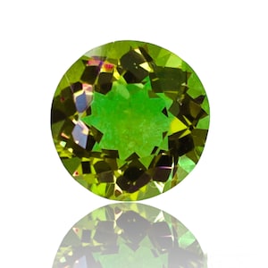 May include: A round, green gemstone with a star-shaped pattern inside. The gemstone is reflecting light, creating a rainbow effect.