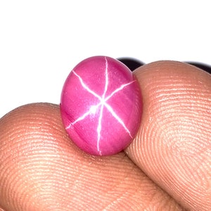 May include: A pink star ruby cabochon gemstone with a white star in the center.