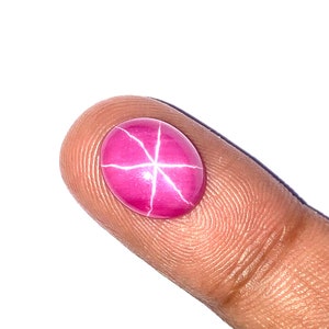 May include: A pink star ruby gemstone with white inclusions, set in an oval cabochon cut.
