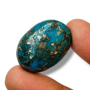 Puede incluir: Un cabujón de turquesa ovalado y liso, de color azul verdoso con motas doradas. La piedra mide aproximadamente 2,5 cm de largo.