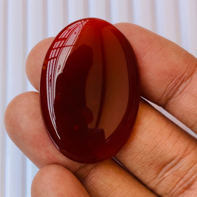 Puede incluir: Una piedra de cornalina lisa de forma ovalada, de color rojo oscuro. La piedra est&aacute; pulida y tiene un acabado brillante.