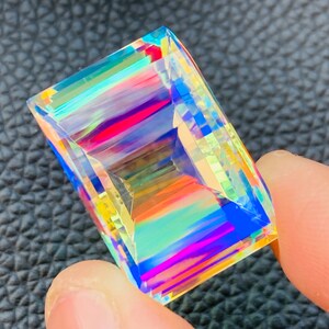 May include: A clear, faceted gemstone with rainbow iridescent colors. The gemstone is cut in a rectangular shape.