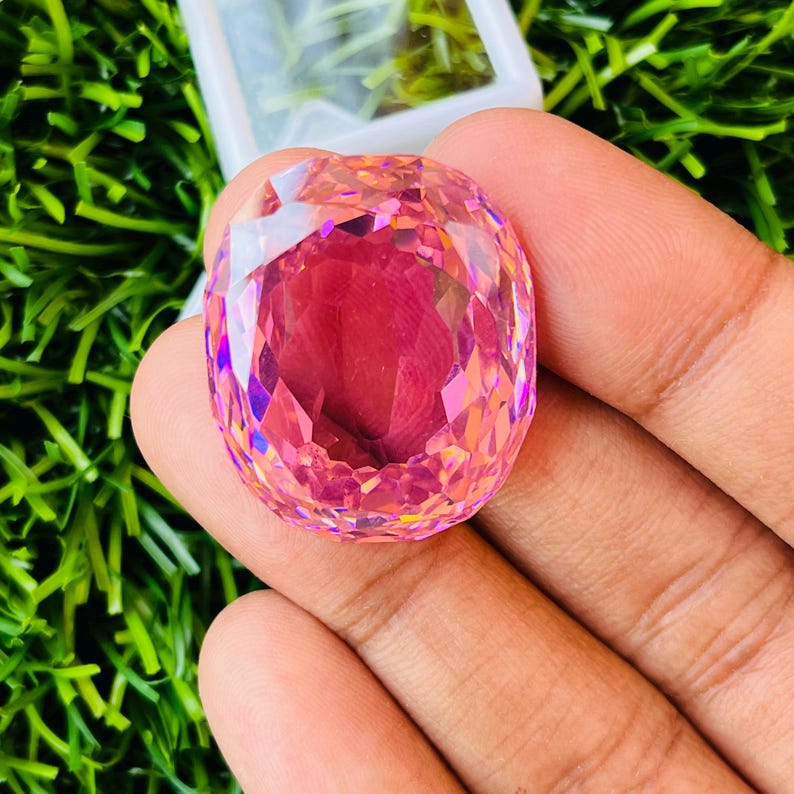 Peut inclure: Une grande pierre pr&eacute;cieuse rose de forme ovale avec une taille facet&eacute;e. La pierre pr&eacute;cieuse a une teinte rose clair avec une l&eacute;g&egrave;re teinte violette. La pierre pr&eacute;cieuse est tenue dans une main.
