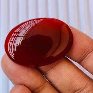 Puede incluir: Una piedra de cornalina lisa de forma ovalada, de color rojo oscuro. La piedra est&aacute; pulida y tiene un acabado brillante.