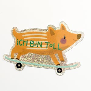Pode incluir: Um adesivo brilhante de um porco de desenho animado vestindo uma camisa listrada e andando de skate. O porco é laranja e tem o nariz rosa. O texto "ICH BIN TOLL" está escrito na camisa do porco em verde.
