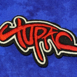 May include: Red and black embroidered patch with the word "UPTC" in a stylized font.