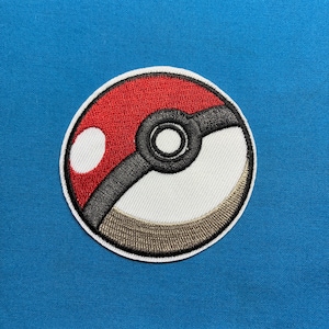 May include: A circular embroidered patch featuring a classic red and white ball design. The top half is red with a white circular highlight, while the bottom half is white with a tan shadow. A thick black band crosses the center with a central button.