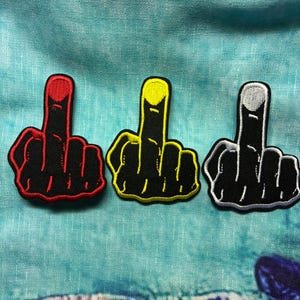 May include: Three embroidered patches in the shape of a hand giving the middle finger. The patches are black with red, yellow, and silver accents. The patches are on a blue background.