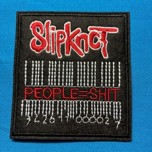 May include: A rectangular black embroidered patch featuring the red Slipknot logo at the top. Below the logo is a white stitched barcode design with the red text PEOPLE=SHIT in the centre and white numerical digits at the bottom edge.