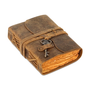 May include: A brown leather journal with a distressed finish, featuring a wrap-around leather strap closure and a metal key charm. The journal has visible side stitching and deckled-edge pages. The text RETQA HANDMADE GENUINE & PREMIUM LEATHER GOODS is printed on the cover.