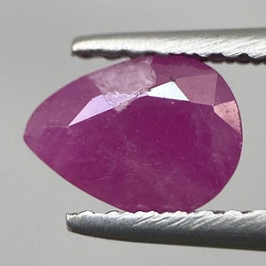 May include: A pink pear-shaped gemstone with facets, held in tweezers.