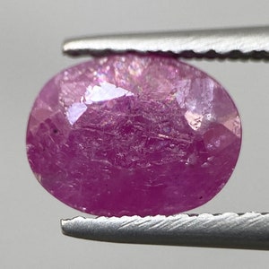 Könnte beinhalten: Ein rosafarbener ovaler Edelstein mit facettiertem Schliff. Der Edelstein hat ein leicht trübes Aussehen mit sichtbaren Einschlüssen.