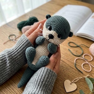 Peut inclure: Une petite loutre en crochet faite à la main, dotée d'un corps bleu sarcelle foncé et d'un ventre ainsi qu'un visage de couleur crème. L'animal en peluche possède des yeux noirs ronds, un petit nez noir et des moustaches en fil blanc.