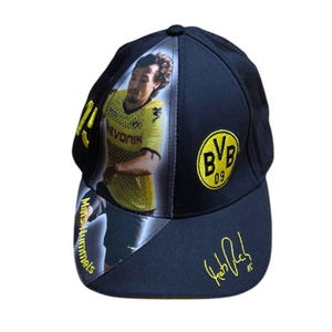 May include: Black baseball cap with a photo of a footballer in a yellow jersey. The cap displays the BVB 09 logo and a gold signature. The brim features the player's name in gold.