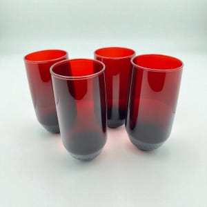 Pode incluir: Quatro copos para beber tingidos de vermelho. Os copos têm um efeito gradiente, passando de um vermelho profundo no topo para uma base mais escura, quase preta. Os copos são cilíndricos com uma base ligeiramente arredondada.