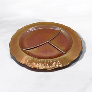 Puede incluir: Un plato de servir dividido con un borde festoneado. El plato está hecho de vidrio iridiscente de color marrón rojizo.