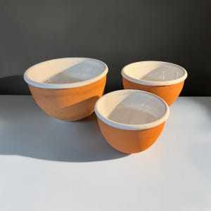 May include: A set of three round bowls featuring a natural terracotta exterior and a smooth, glossy white interior finish. Each bowl has a thick, rounded rim and a deep, curved basin, arranged in a cluster with varying sizes for food preparation.