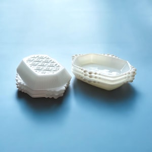 Może przedstawiać: Dwa białe naczynia z mlecznego szkła, jedno z falistym brzegiem, a drugie z wzorem wafelkowym. Oba naczynia wykonane są z delikatnego, prześwitującego materiału.