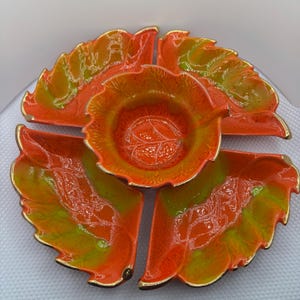May include: A set of four orange and green ceramic serving dishes with gold trim. The dishes are shaped like leaves and have a raised design. The set includes a central bowl and three smaller dishes.