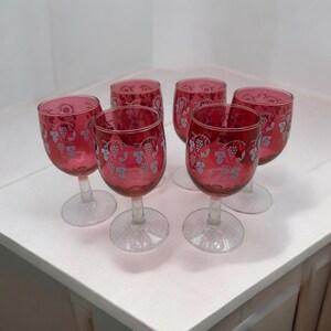 May include: Six stemmed wine glasses with a ruby red color and a white grapevine design.