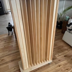Peut inclure: Un panneau acoustique en bois haut avec des lattes verticales. Le panneau est sur roulettes et a une finition en bois clair.