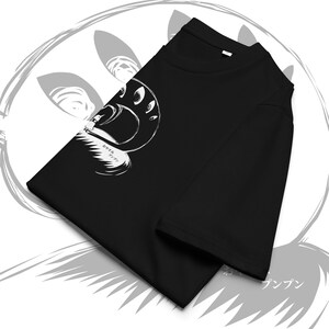 May include: Black t-shirt featuring a white illustration of a stylized face with multiple eyes and the Japanese text "Oyasumi Punpun". The design is a minimalist, graphic style. The shirt is folded, showcasing the design prominently.