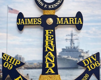 May include: Navy blue wooden anchor with gold accents and text. The anchor reads "USS John F. Kennedy", "Jaimes Maria", "Fernanda", "Ship 09 PIR", "Div 106", and "03-12-2026". A gold rope wraps the anchor's center, and a Navy emblem is at the bottom.