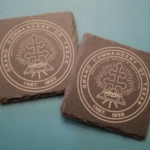 May include: Two black slate coasters with a white engraved design. The design features a skull and crossbones with the text "Grand Commandery of Texas Inst. 1855".