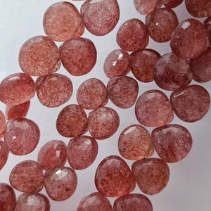 May include: A strand of pink and red gemstone beads. The beads are faceted and have a slightly irregular shape. They are strung on a clear thread.
