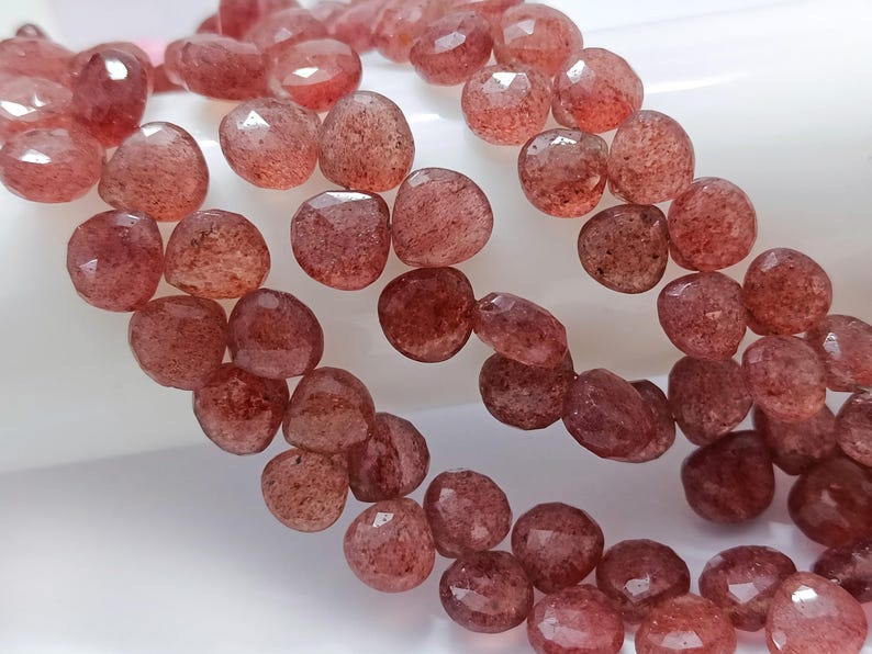May include: A strand of faceted, reddish-brown gemstone beads. The beads are round and have a slightly irregular shape.