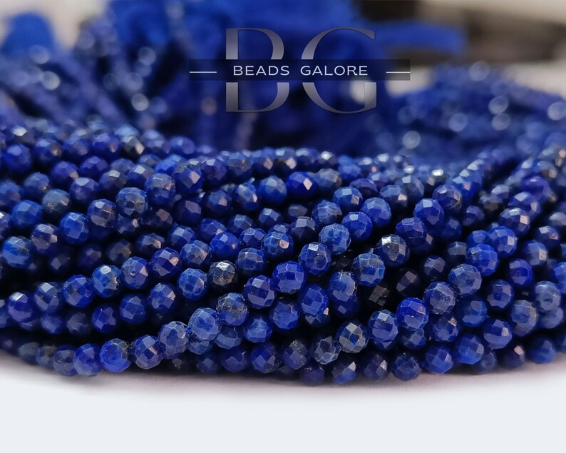 May include: A strand of deep blue lapis lazuli beads, each bead is faceted and round, the beads are strung together to form a long strand.