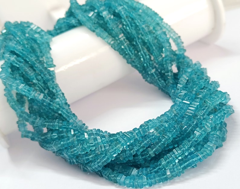 Op de afbeelding: Een bundel kleine, vierkant geslepen, lichtblauwe edelstenen. De edelstenen zijn aan elkaar geregen en vormen een dikke, gedraaide streng. De kleur is een helder, helder turquoise en de stenen lijken gepolijst.